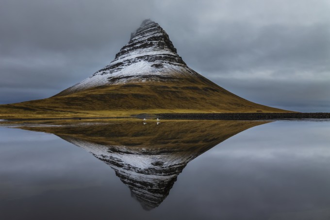 Kirkjufell and Whooper swans (Cygnus cygnus), Vesturland, Iceland With the right amount of snow an 'eye' is revealed in the side of a mountain. It almost looks like the eye in the pyramid on the dollar bill. As I photographed a pair of swans took flight.
