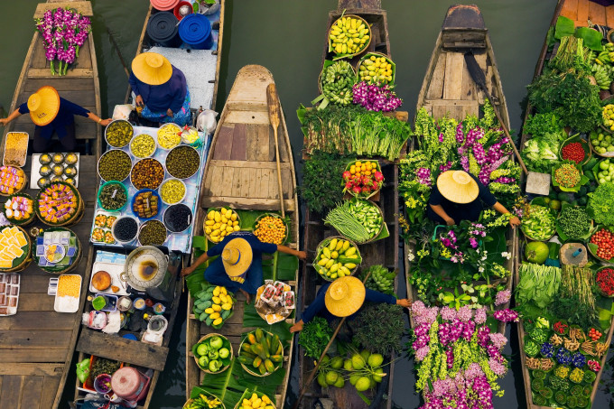 Floating markets are a common tradition throughout Southeast Asia where the numerous rivers and waterways are a primary means of transportation and commerce between villages. In this overhead view, Bangkok vendors draw their boats together to exchange a colorful, tasty array of goods, Thailand.